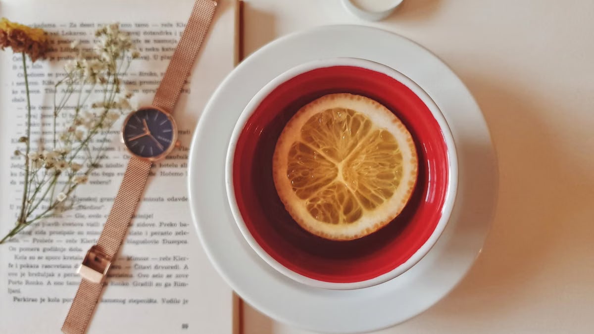 A warm still life of tea with lemon, a watch, and a book, creating a relaxing atmosphere indoors.