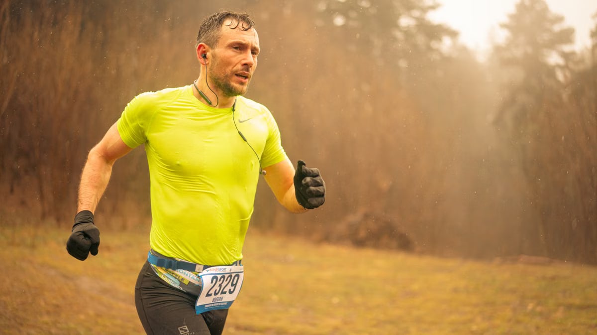 Fit adult man running in a cross country race wearing neon sportswear and gloves, captured in motion outdoors in Brașov.